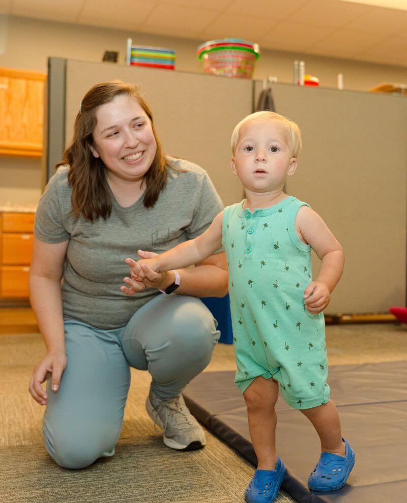 Therapist holding hands with toddler.